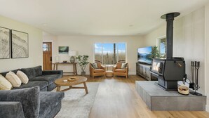 A modern living room with a fireplace, grey sofas, wooden coffee table, and a view of the outdoors. - NEW Secluded Hillside Retreat on 10 acres with Stunning Views (Port Angeles)