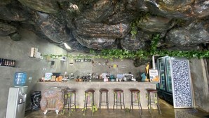 Een bar met een rustieke stenen plafond, barstoelen en een aanrecht met diverse spullen.