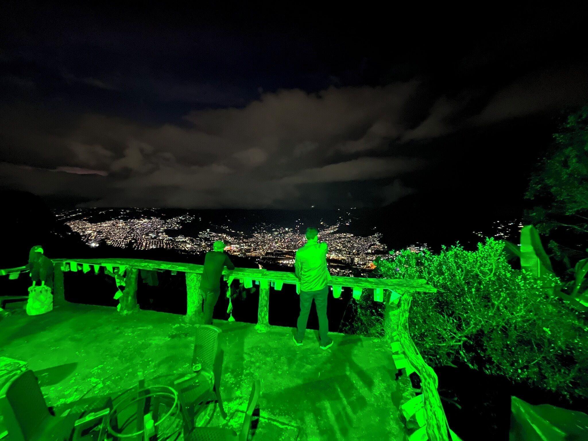 A nighttime view from a balcony overlooking a cityscape with a person standing on the edge.