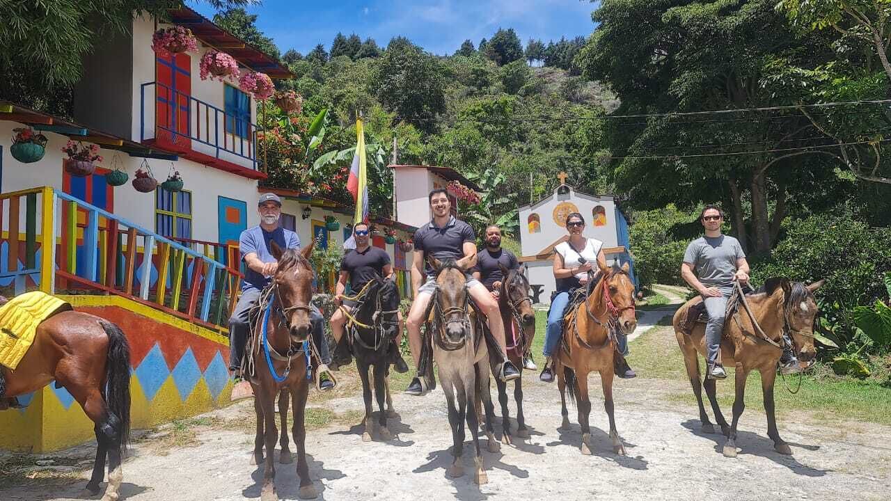 A group of people riding horses on a dirt path with colorful buildings in the background.