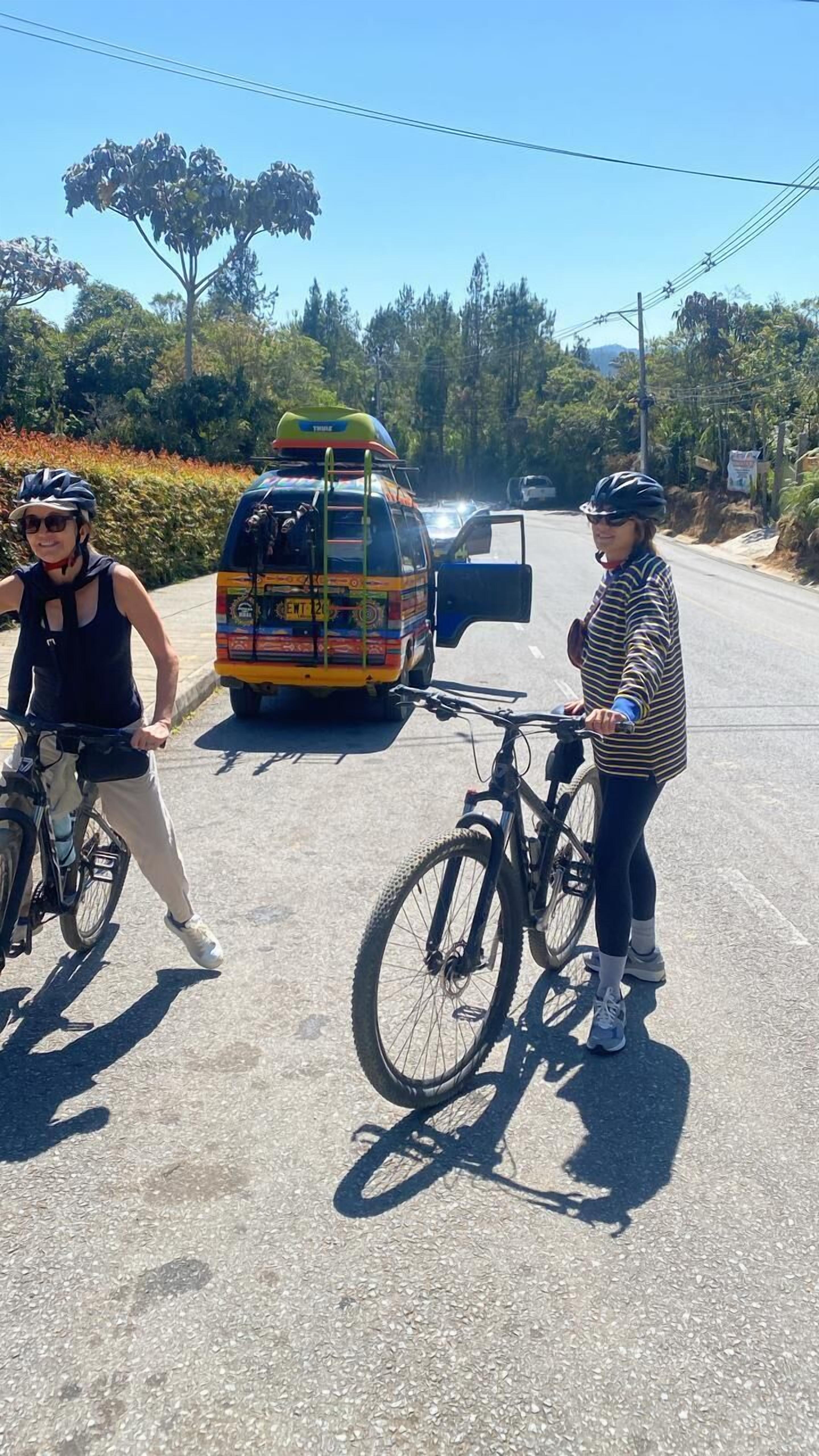 Deux personnes à vélo sur une route, avec un autobus aux couleurs vives en arrière-plan.