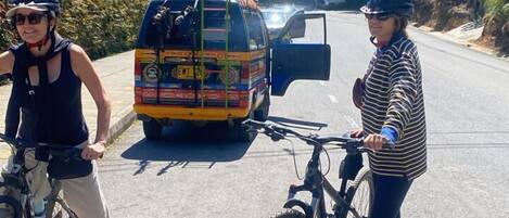 Deux personnes à vélo sur une route, avec un autobus aux couleurs vives en arrière-plan.