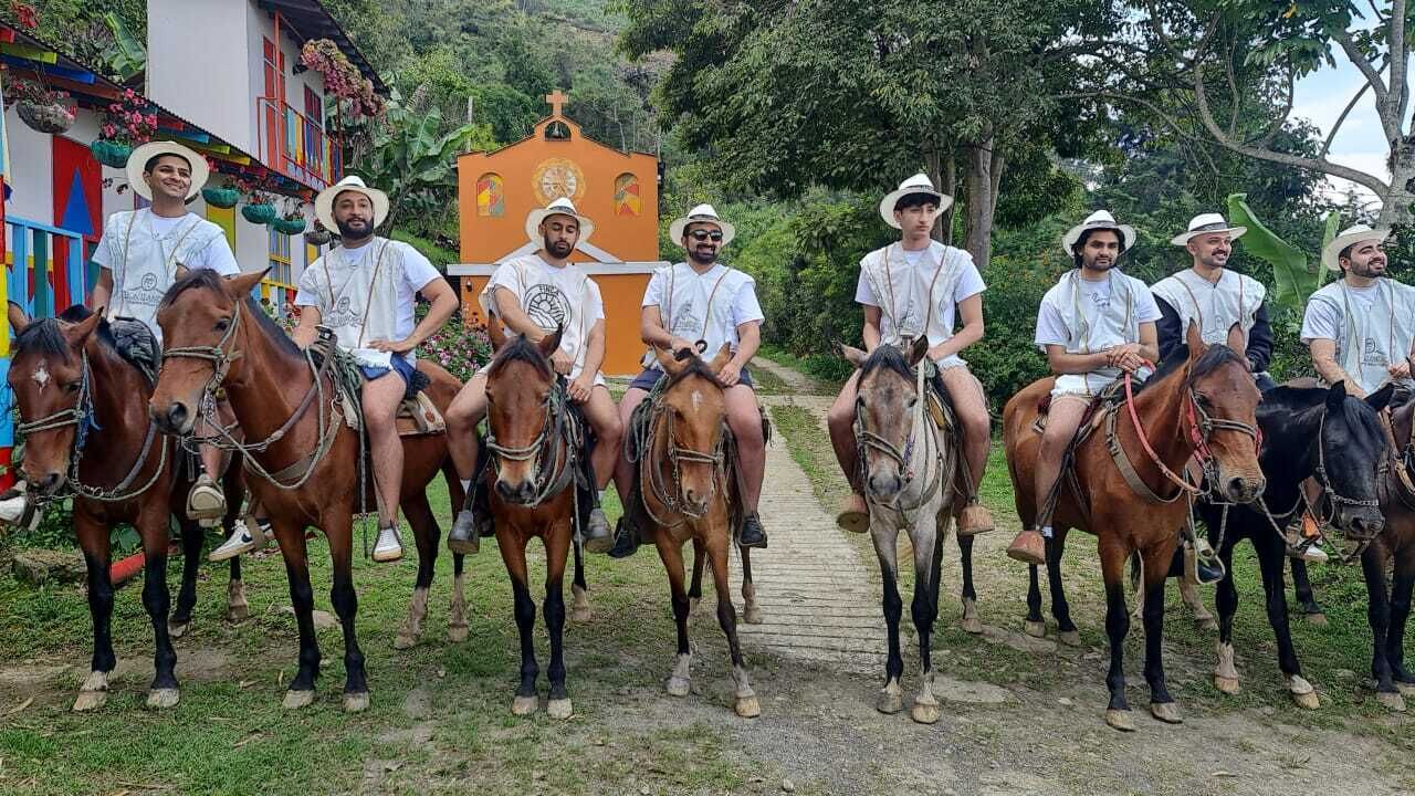 A group of people on horseback in front of a building with colorful walls and a cross on top.