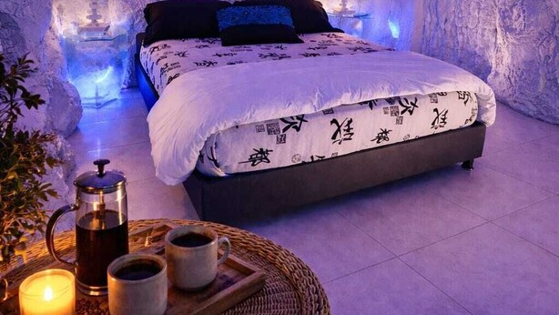 Een slaapkamer met een bed, kussens, een nachtkastje met een lamp, en een dienblad met koffiekopjes en een theepot.