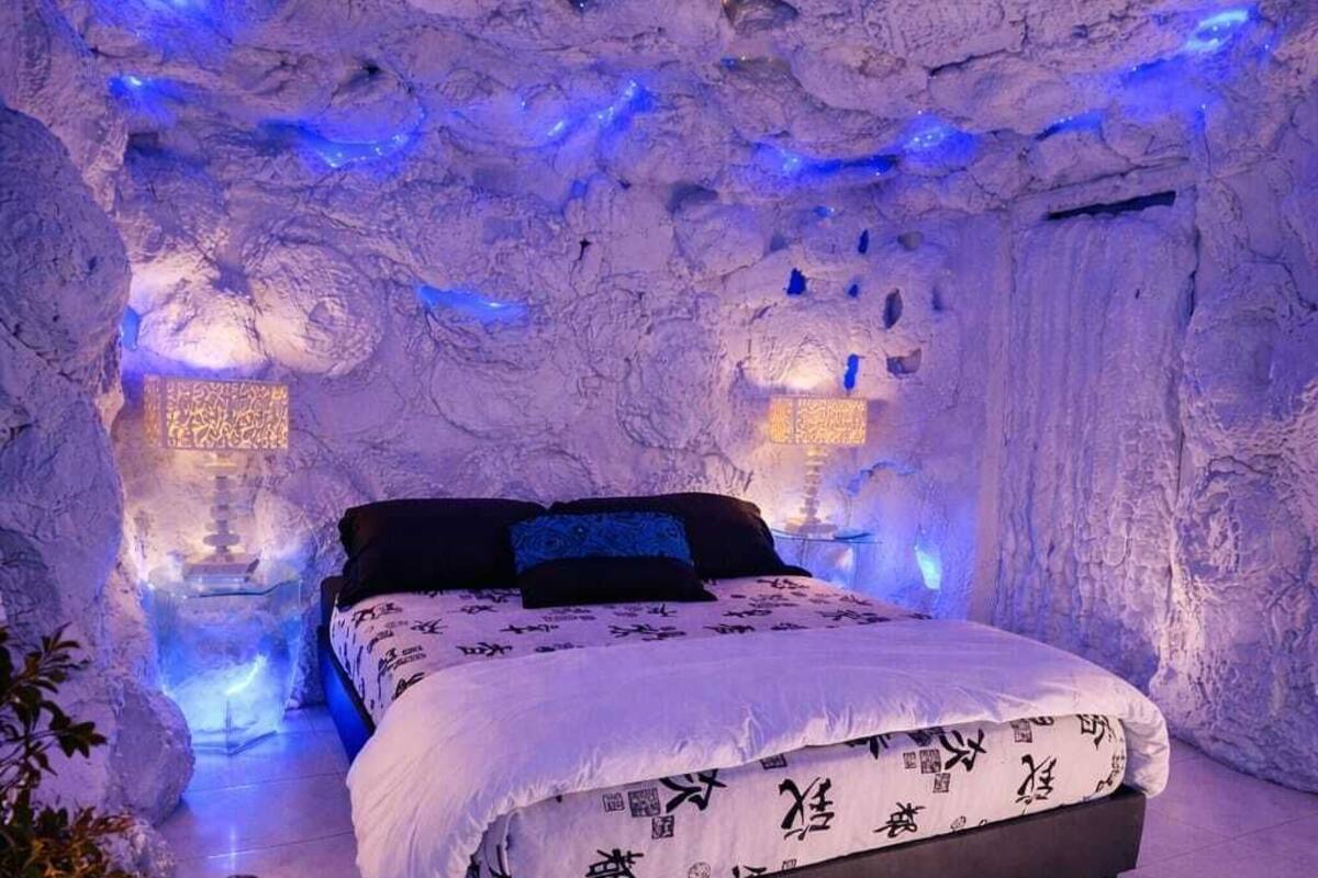 Une chambre à coucher avec un lit, des oreillers, une table de chevet avec une lampe, et un plateau avec des tasses à café et une théière.