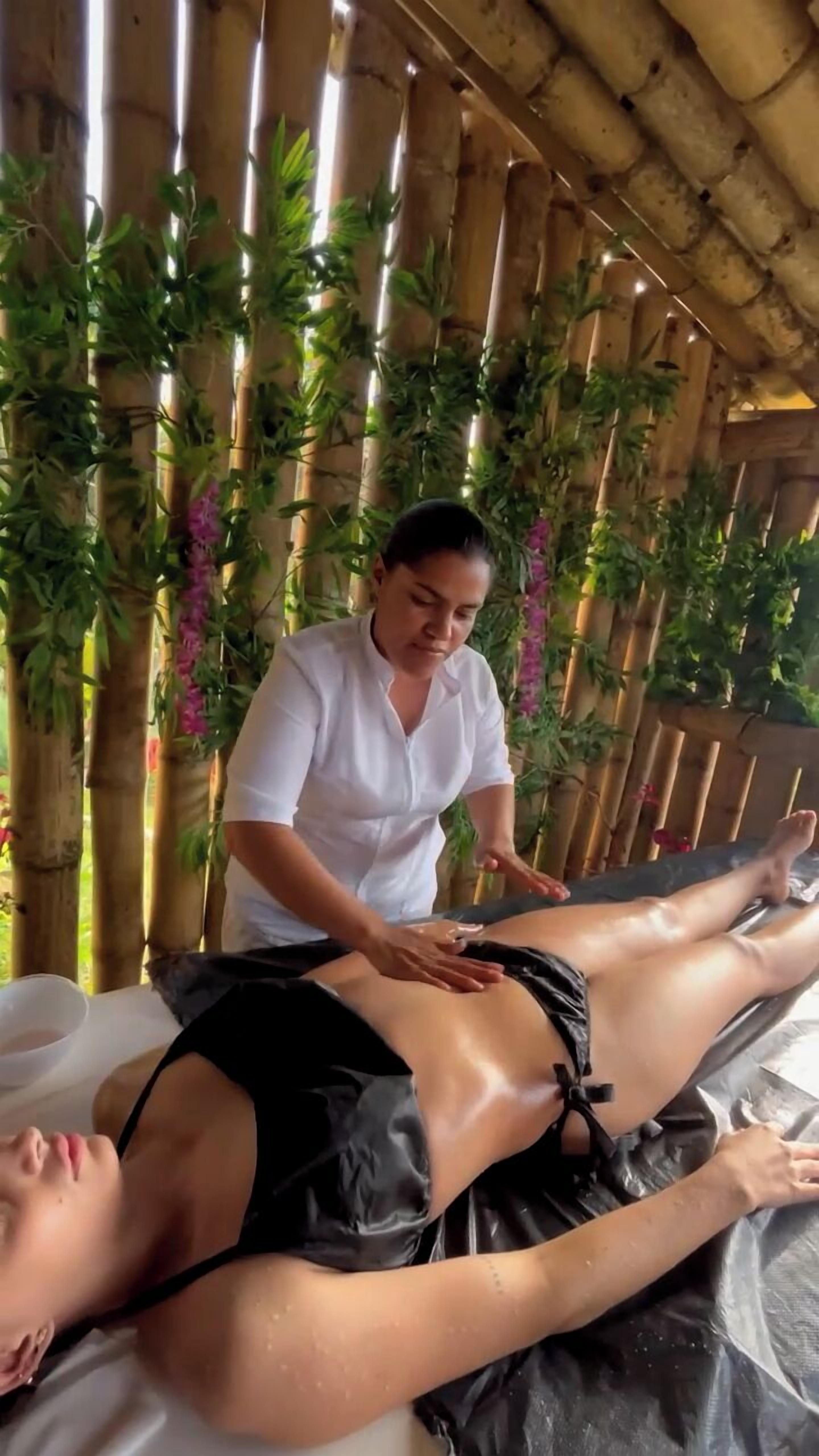 A person receiving a massage in a room with bamboo walls and hanging plants.