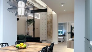 Un comedor moderno con una mesa de madera, sillas negras y un frutero. Hay una lámpara colgante negra sobre la mesa.
