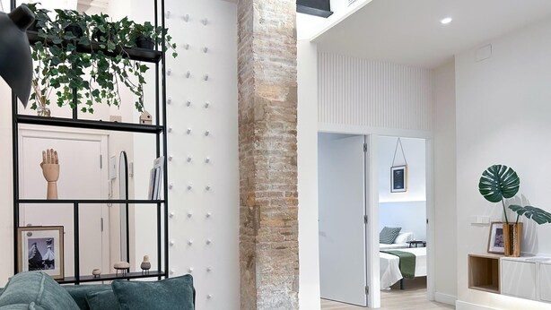 Una sala de estar moderna con un sofá verde, una mesa de centro de vidrio y una estantería con objetos decorativos.