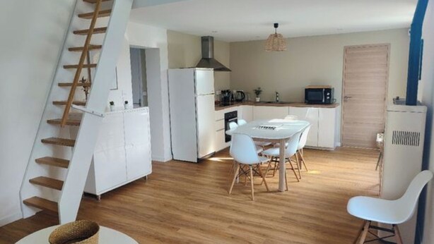 Una cocina moderna con armarios blancos, una mesa de comedor con sillas, una escalera y una pequeña mesa redonda con una cesta.