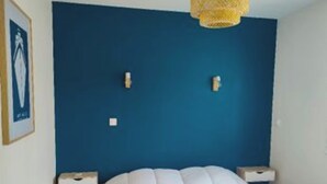 Un dormitorio con una pared azul de acento, una cama blanca, dos mesitas de noche y una lámpara colgante.