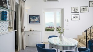 A modern kitchen with a round table, blue chairs, and a view of the sea through a glass door. - Estate4home- Casetta Arienzo (Positano)