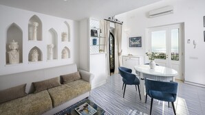A modern living room with a sofa, a coffee table, and a dining area with chairs and a table. - Estate4home- Casetta Arienzo (Positano)