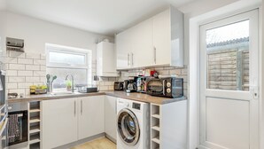 A compact kitchen with white cabinets, a built-in washing machine, a microwave, and a sink. - Beautiful House in North London with Parking (London)