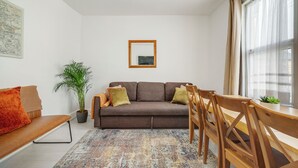 A modern living room with a brown sofa, wooden chairs, a potted plant, and a colorful rug. - Beautiful House in North London with Parking (London)