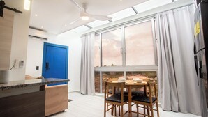 Een moderne keuken met een blauwe deur, een eethoek met een tafel en stoelen, en een groot raam met gordijnen.