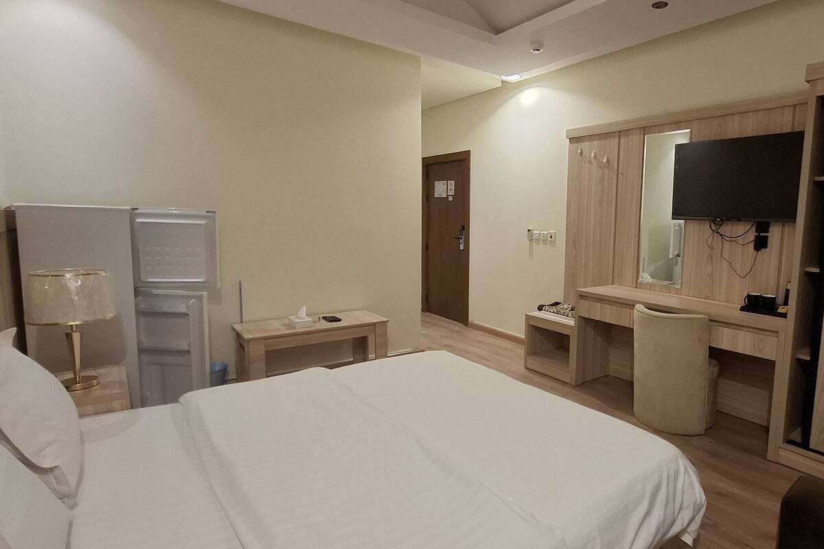 Una habitación de hotel con cama, escritorio, silla, televisor y armario.