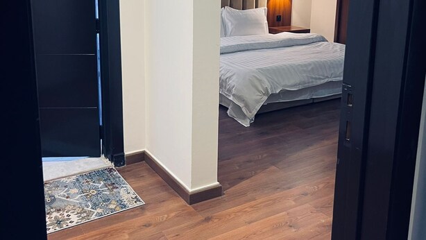 Een hotelkamer met een houten vloer, een bed met wit beddengoed, een nachtkastje en een wandlamp.