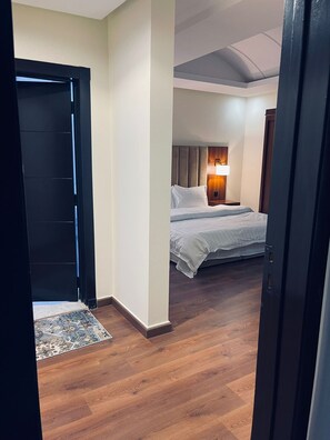 Ein Hotelzimmer mit Holzboden, einem Bett mit weißer Bettwäsche, einem Nachttisch und einer an der Wand befestigten Lampe.