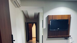Een hal met houten vloer, een tv aan de muur en een deur links.
