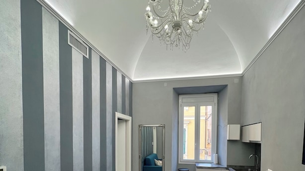 Ein modernes Wohnzimmer mit einem blauen Sofa, einer Kristallleuchtre und einer Küchenzeile mit Esstisch und Stühlen.