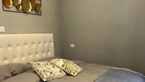 Ein Schlafzimmer mit einem gepolsterten Kopfteil, einer grauen Bettdecke, gemusterten Kissen und einer Wanddekoration.