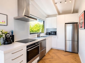 Una cocina moderna con electrodomésticos de acero inoxidable, armarios blancos y una ventana con vistas a zonas verdes.