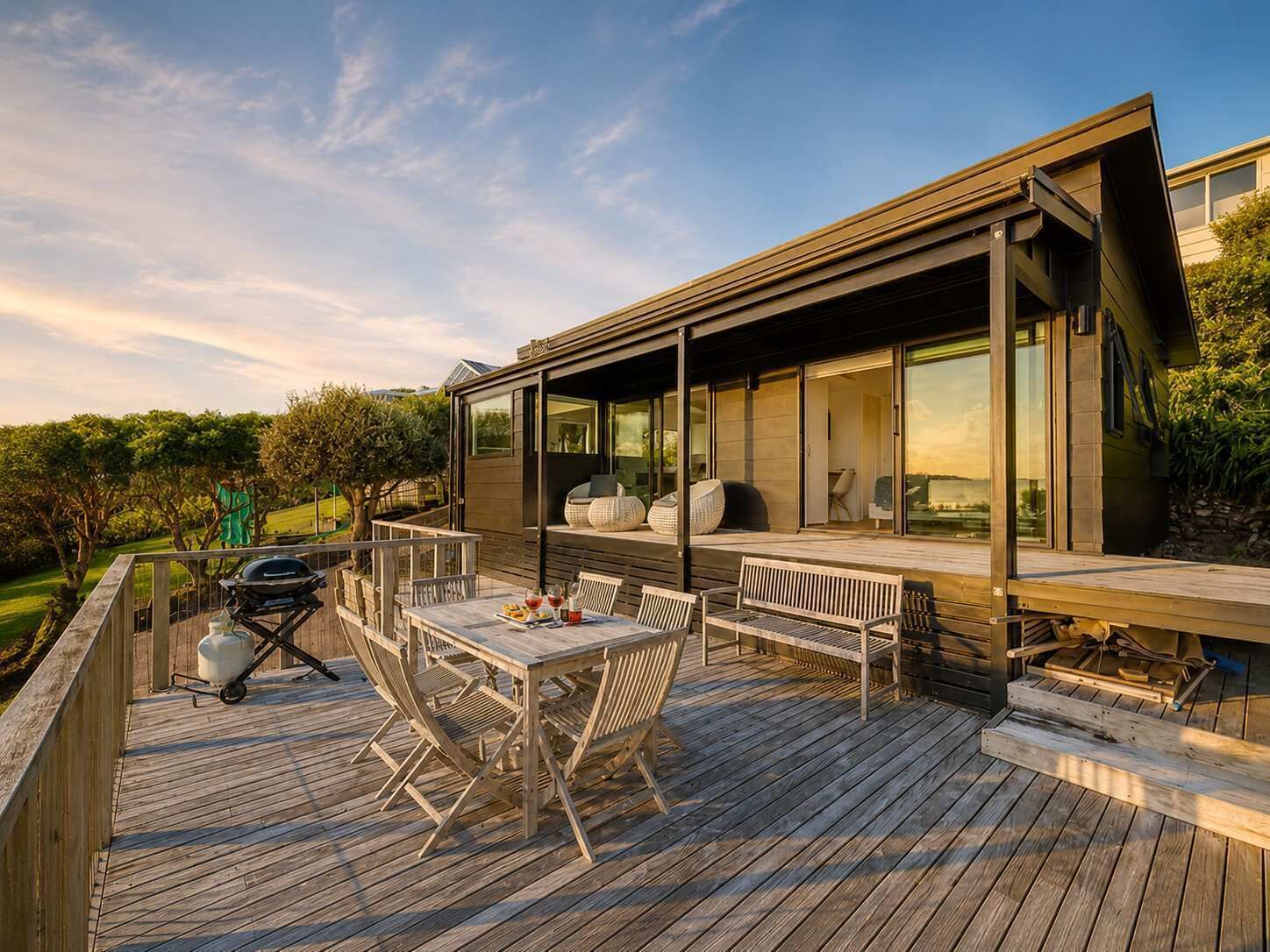 A modern house with a wooden deck, outdoor seating, and a barbecue grill.