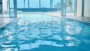 An indoor swimming pool with clear glass walls, a view of palm trees, and exit signs. - Discounted GroundFloor. King Bed. Queen Bunks.Twin bunks. Wheelchair Accessible. (Orange Beach)