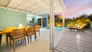 Eine Terrasse im Freien mit Esstisch und Stühlen, ein Poolbereich mit Liegestühlen und ein überdachter Gang.