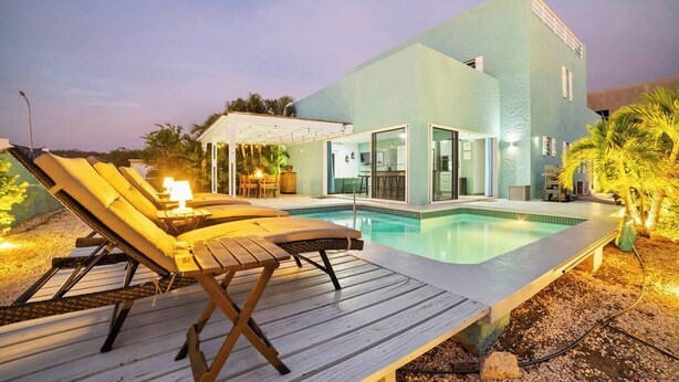 Ein modernes Haus mit Swimmingpool, Liegestühlen und einer überdachten Außenbereich.
