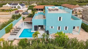 Una casa moderna de dos pisos con piscina, rodeada de vegetación y otras viviendas.