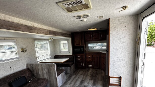 A compact RV interior with a kitchenette, a seating area with a sofa, and a window providing natural light.