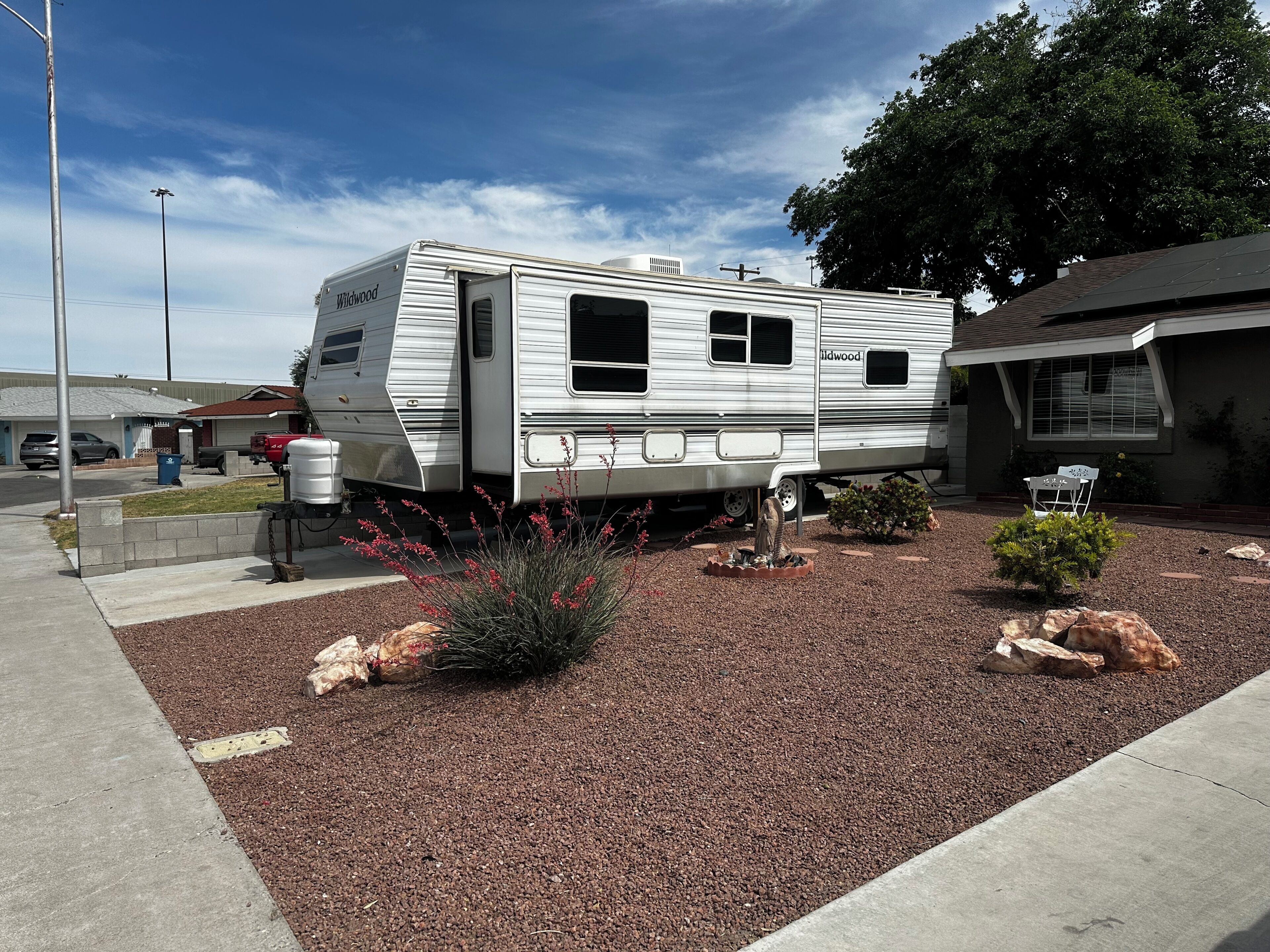 A mobile home with a water tank, a small garden with red flowers, and a paved driveway.