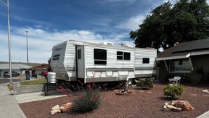 A mobile home with a water tank, a small garden with red flowers, and a paved driveway.