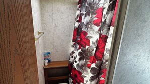 A compact bathroom with a toilet, a shelf with toiletries, and a shower curtain with a floral pattern.