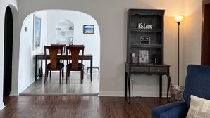 Ein Essbereich mit Tisch und Stühlen, ein Bücherregal mit einem Schild ‚Relax‘ und einer Lampe.