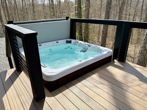 Ein Whirlpool auf einer Holzterrasse mit Metallgeländer, umgeben von Bäumen.