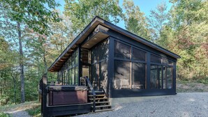 A modern cabin with large windows, a hot tub, and a gravel driveway. - The Briar House-A modern retreat in Hocking Hills (McArthur)