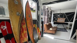 A room with surfboards against the wall, a couch, and a painting on the wall. - Pousada e Hostel Natal Free Surf (Natal)