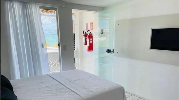 A hotel room with a bed, a TV mounted on the wall, and a fire extinguisher visible through the door. - Pousada e Hostel Natal Free Surf (Natal)