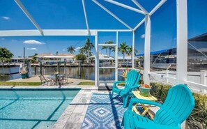 Un espace piscine avec des chaises turquoise et une vue sur un port de plaisance.