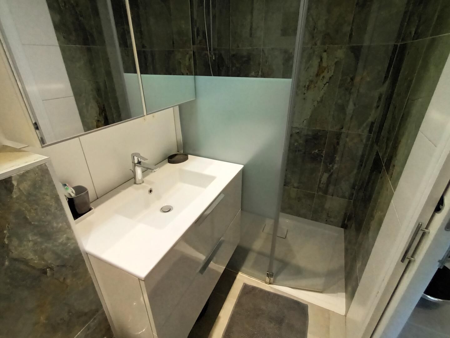 A modern bathroom with a white sink, a mirror, and a shower enclosure.