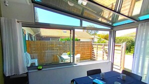 A sunlit room with a table and chairs, large windows, and a view of a backyard. - Gîte Charles - CAPBRETON (CAPBRETON)
