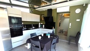 A compact kitchen with modern appliances, a dining area with a table and chairs, and a visible clock on the wall. - Gîte Charles - CAPBRETON (CAPBRETON)