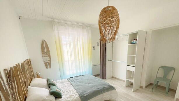 A bedroom with a bed, a wardrobe, a chair, and a hanging light fixture. - Close to the beach! Family home with a large patio/garden—sleeps 9 (Longeville-sur-Mer)