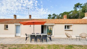 A patio with a table and chairs, an umbrella, and a view of a building with a tiled roof. - Close to the beach! Family home with a large patio/garden—sleeps 9 (Longeville-sur-Mer)