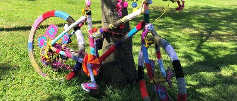 A colorful, crocheted bicycle leaning against a tree in a grassy area.