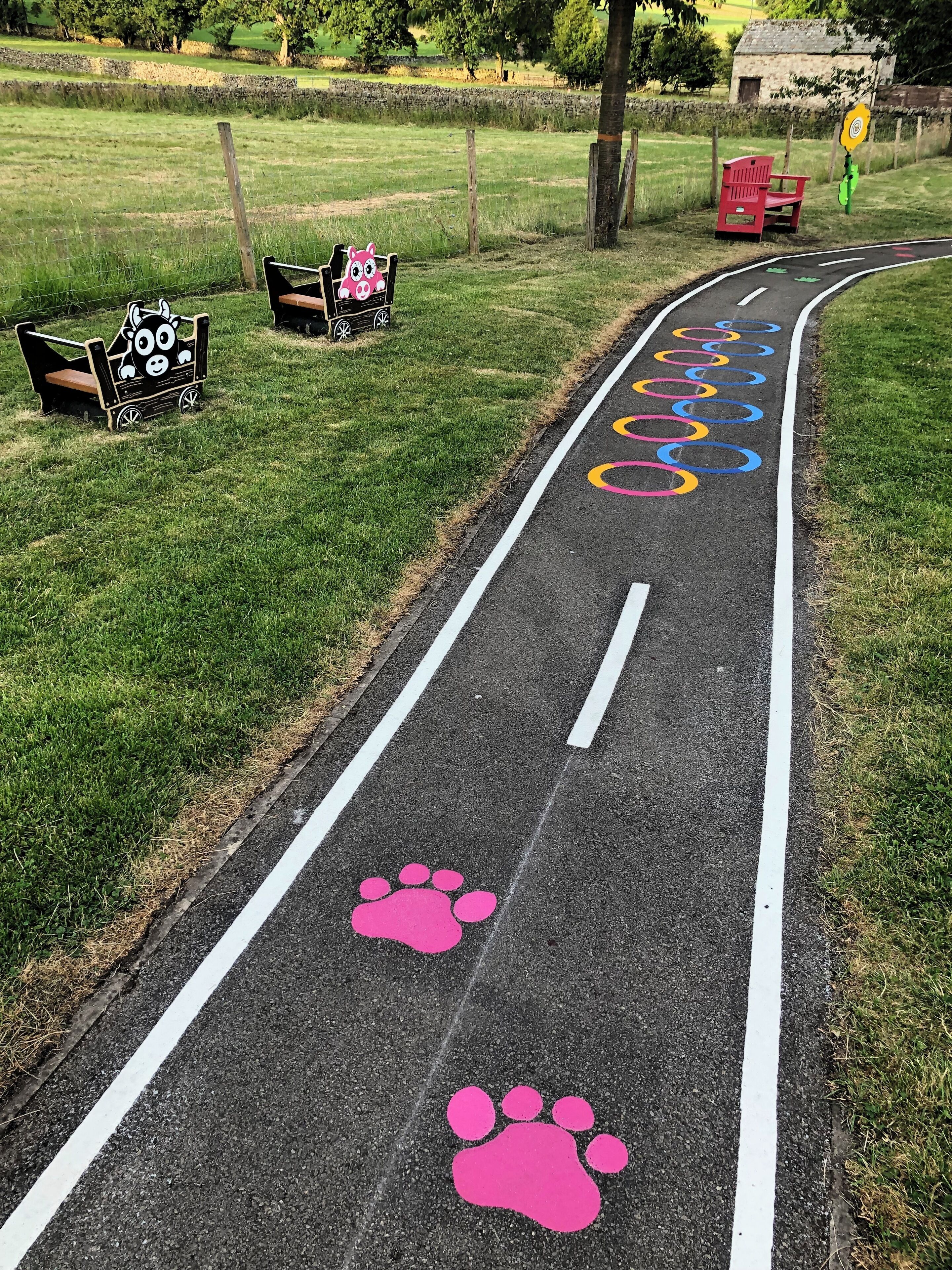 A paved path with colorful markings and a pink paw print symbol.
