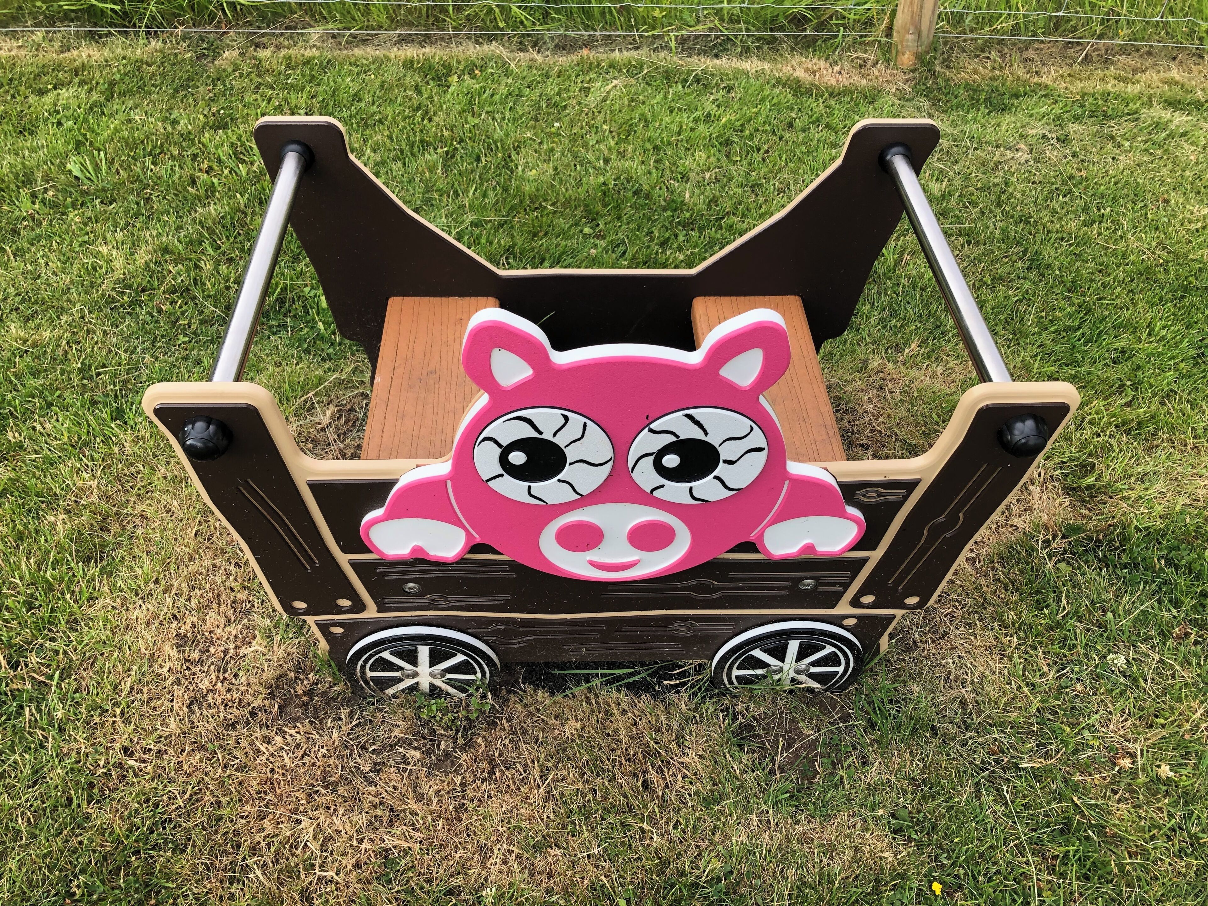 A pink piggyback carrier with a wooden seat and metal wheels.