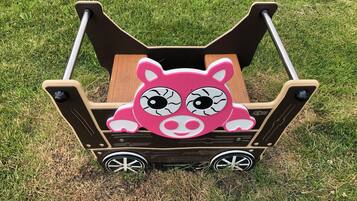 A pink piggyback carrier with a wooden seat and metal wheels.